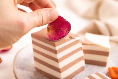 Cocoa and milk jelly with dried apricots with hand on white wooden background and linen textile,