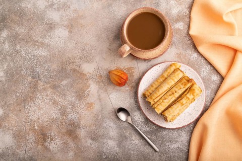 Waffles with caramel on brown concrete background and orange linen textile, cup of coffee, top