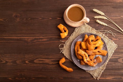 Crunchy biscuit Brushwood cookies sprinkled with powdered sugar on brown wooden background and