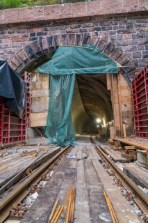 Ansicht eines Tunnels mit sichtbaren Schienen und Baugerüst, beleuchtet durch Baustellenlampen, Bau