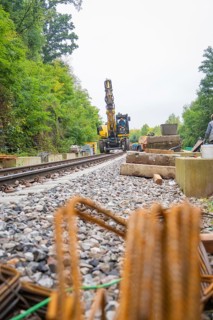 Baustelle mit Bahnschienen und Bagger in einer von Bäumen umgebenen Umgebung, sichtbar sind