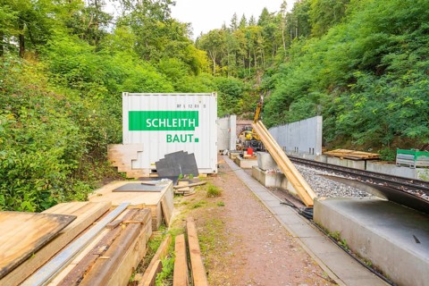 Schleith Baustellencontainer neben Schienen und Materialstapeln im Grünen, Bau der Hermann