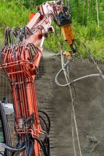 Industrielles Baugerät sprüht Beton auf strukturierten Untergrund umgeben von Vegetation, Bau der