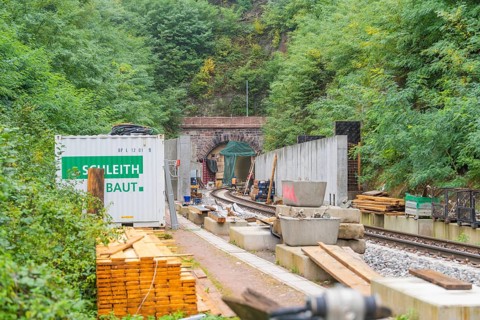 Tunnelbaustelle mit Materialien und einem fernen Eingang umgeben von Wald, Bau der Hermann