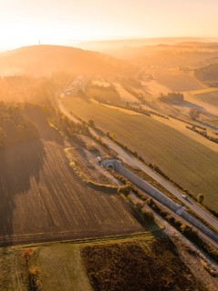 Landschaft während eines Sonnenaufgangs mit Feldern, Hügeln und einer Straße, die von goldenem