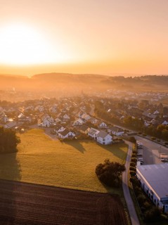 Dorfansicht bei Sonnenaufgang mit beleuchteten Dächern und umliegenden Feldern, Gechingen,