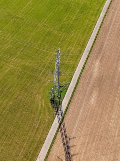 Luftbild eines Strommasts auf einer Wiese, umgeben von Feldwegen und langen Schatten, Nagold,