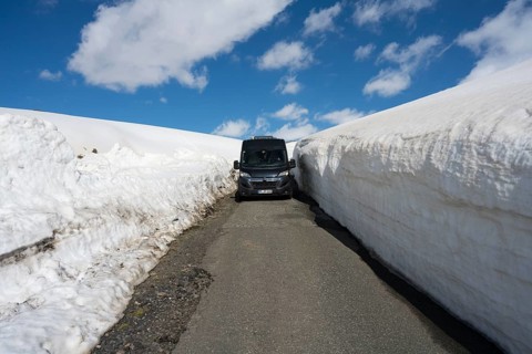 Van auf schmaler Straße zwischen hohen Schneemauern mit blauem Himmel, mit dem Camper zum Aragaz,