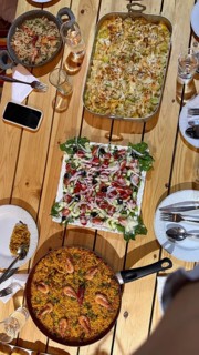 Rustic wooden table set with multiple homemade dishes including a large pan of seafood paella, a