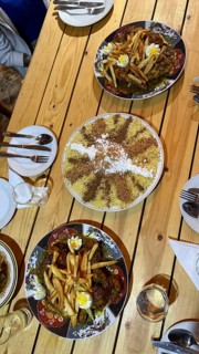 Table spread of moroccan dishes for sharing, chicken tajine topped with fries and eggs, sweet seffa