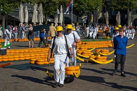 Träger in weißen Anzügen und gelben Hüten tragen Käse auf einem traditionellen Markt unter einer