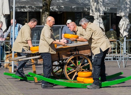 Männer in beiger Kleidung stapeln Käseräder auf einem traditionellen Holzwagen, Käse, Käsemarkt,