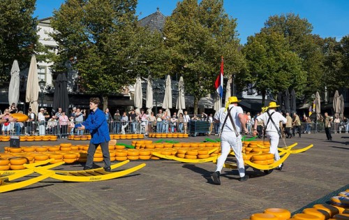 Männer in traditionellen Trägeranzügen auf einem Käsemarkt unter einer niederländischen Flagge,