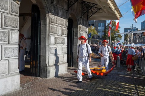 Männer mit Käse laufen durch ein historisches Marktgelände mit Publikum, ehemalige Stadtwaage,