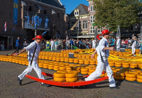 Männer mit roten Hüten tragen Käse durch einen belebten, sonnigen Stadtmarkt, Käseträger, Käse,