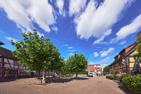Platz, Fachwerkhäuser, Restaurant Die Scheuer, Gehweg aus Betonpflastersteinen, Bäume, blauer