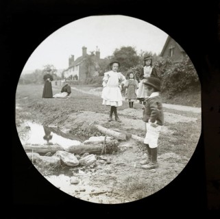 Magic lantern slide of mothers with children outside playing by a stream in a village rural