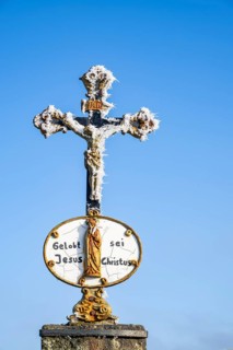 Crucifix with hoarfrost in front of blue sky at sunshine in winter, Bavaria, Germany