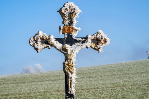Crucifix with hoarfrost in front of blue sky at sunshine in winter, Bavaria, Germany