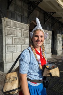 Woman in traditional dress and headdress smiling in front of a historic building, former city weigh