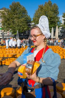 Woman in traditional traditional costume selling pieces of cheese at a market in sunny weather,