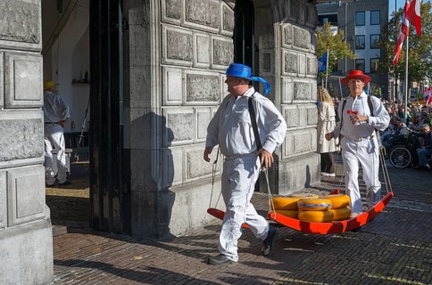 Men in traditional clothing transporting cheese at a historic building, cheese carrier, cheese,