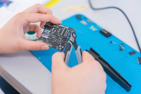 Person uses pliers to work on a circuit board surrounded by electronic parts