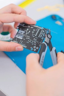 Person holds a circuit board and works on it with pliers on a blue mat