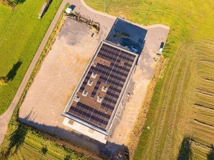 Top view of solar roof of a building with surrounding fields and car park, new building with green