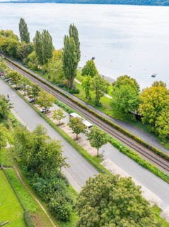 Road and parallel railway line next to a lake, surrounded by trees, Lake Constance Germany