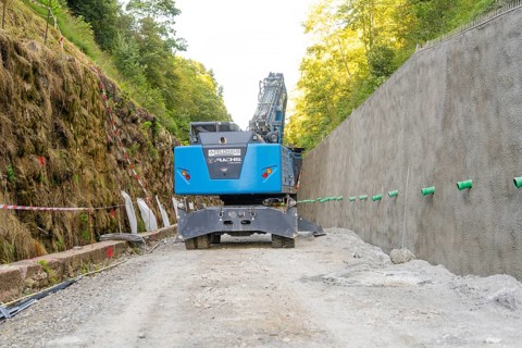 Blue excavator on a construction site between wooded earth slopes, Hermann Hessebahn construction