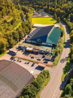 Industrial building with adjacent car park and green landscape, light roof colour, surrounded by a