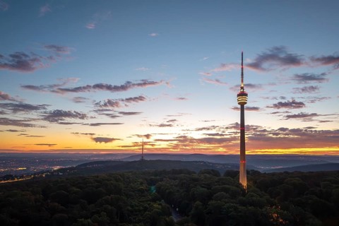 Illuminated television tower rises above forest in the morning red with clouds,