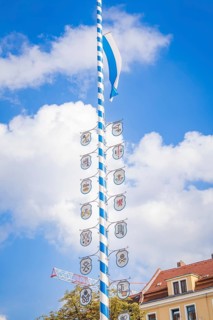 Bavarian maypole with coat of arms in front of blue sky and roof gable, Munich, Germany