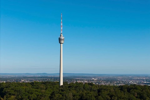 Detailed view of a television tower, embedded in forests, with a wide view of the city under a blue