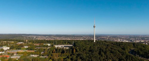 Panoramic view of a cityscape dominated by a television tower and surrounded by dense forests under