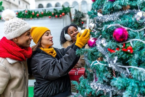 Happy multi ethnic friends gathering at an outdoor christmas market, joyfully decorating a colorful
