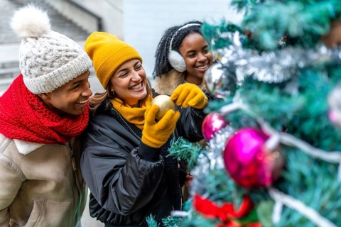 Group of cheerful multi ethnic friends decorating a christmas tree in the city, enjoying winter