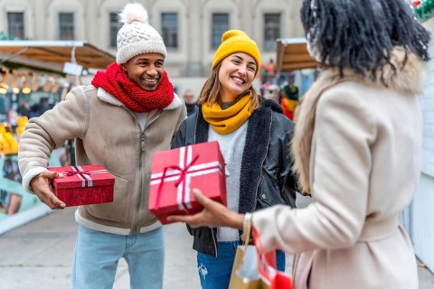Happy friends exchanging christmas gifts at a bustling market, enjoying the festive atmosphere and