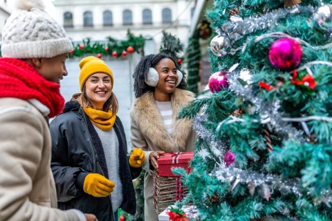 Three happy friends enjoying christmas shopping at an outdoor market, choosing a christmas tree and