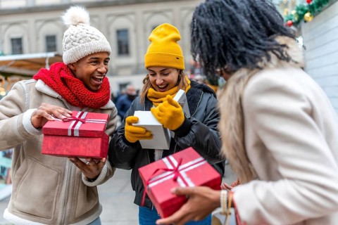 Happy multiethnic friends exchanging christmas gifts at a christmas market in the city center