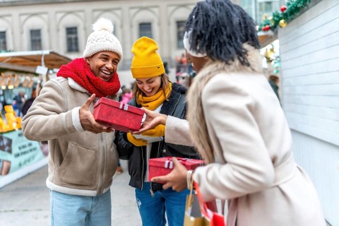 Happy multi ethnic friends exchanging christmas gifts at a christmas market, enjoying winter