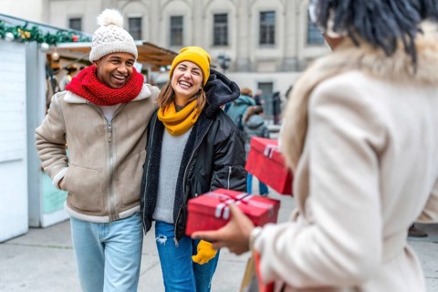 Friends laughing and exchanging christmas gifts at a winter market in the city, enjoying the
