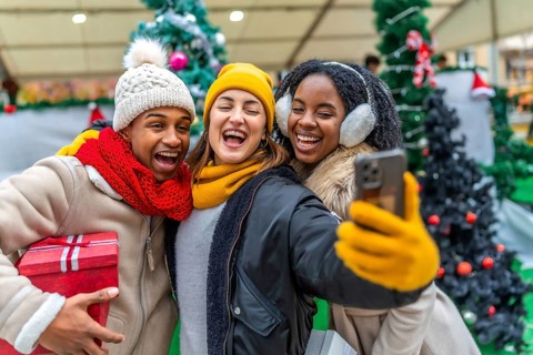 Three cheerful multi ethnic friends taking a selfie at a christmas market while holding a gift,