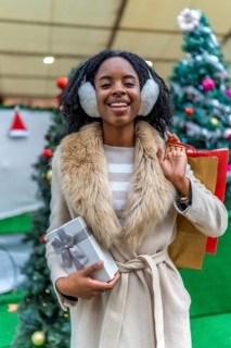 Happy customer holding a christmas present and shopping bags, enjoying winter sales in a decorated