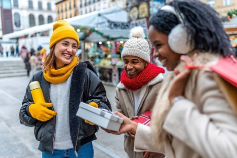 Multi ethnic friends exchanging gifts and smiling at a christmas market during wintertime