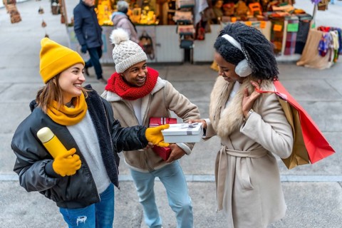 Happy multi ethnic friends joyfully exchanging christmas gifts while shopping together at a