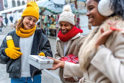 Happy multi ethnic friends exchanging christmas gifts at an outdoor winter market, enjoying the