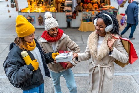 Happy multi ethnic friends exchanging christmas gifts at the christmas market during wintertime