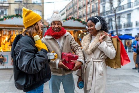 Three friends exchanging christmas gifts and enjoying a warm beverage at a christmas market in the